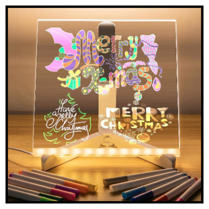 Glowing acrylic LED light box on wooden surface displaying colorful Christmas-themed lettering and designs including Merry Christmas