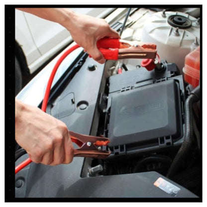 Close-up of person using red jumper clamps to connect red jumper cable to car engine bay with open hood visible