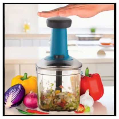 Countertop food chopper with blue handle and clear bowl containing chopped vegetables with hand pressing top button and bell peppers around it on kitchen counter