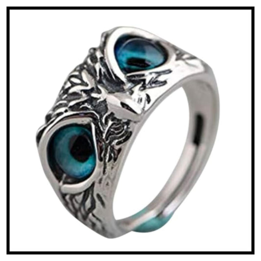 Silver-toned owl eye open ring with large dark teal-blue stone eyes and tree trunk textured design on white background