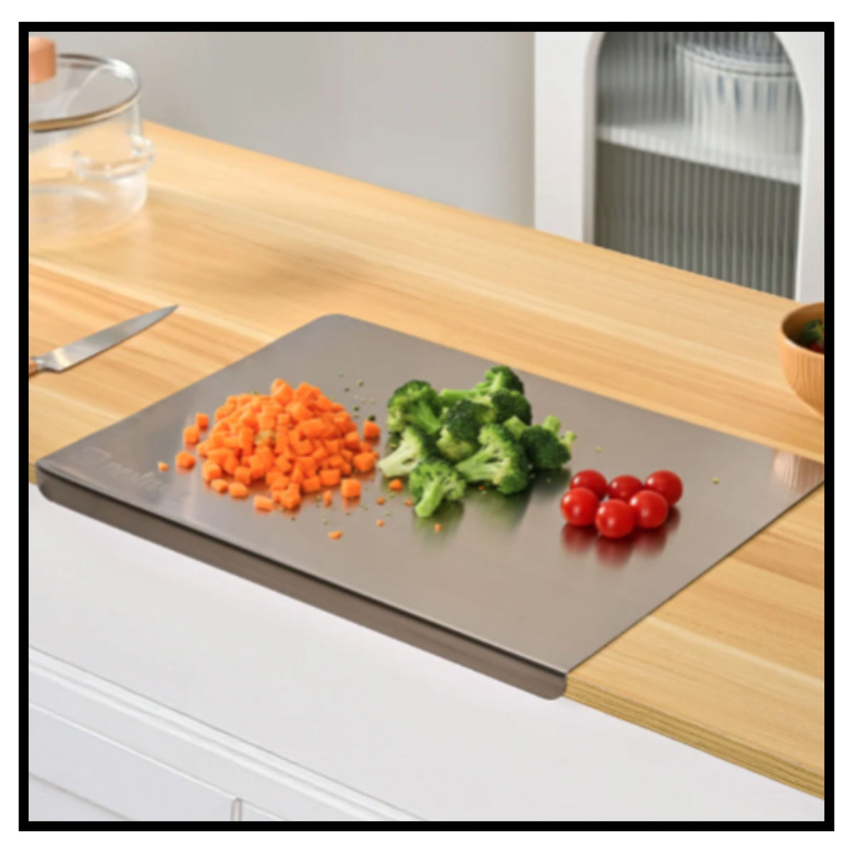 Stainless steel chopping board on kitchen countertop with chopped carrots broccoli and cherry tomatoes
