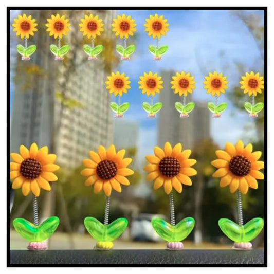 Four yellow shaking head sunflower dancing ornaments with green leaves on car dashboard with blurred outdoor background